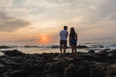 Girl Boy silhouetted beach ocean sunrise morning rocky coastline landscape.の写真素材