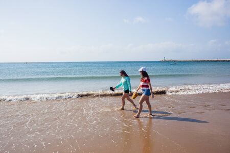 Teenage girls walking beach water line ocean shoreline landscape.の写真素材