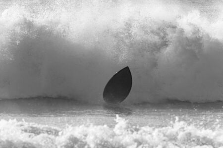 Surfer surfing crashing leaves board and ocean wave dramatic black and white photo.