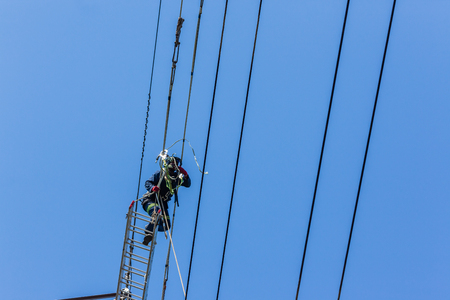 Electricians high up hanging suspended on electrical steel tower installing new high voltage electricity power linesの写真素材