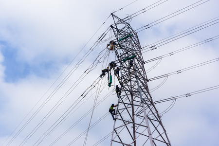 Electricians working on electrical cable power lines on steel tower.の写真素材