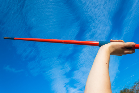 Athletes teenager hand holding red javelin closeup abstract into blue sky.の写真素材