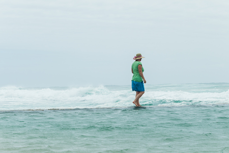 Woman walking beach tidal pool wall watching  ocean waves power crashing on overcast windy day.の写真素材