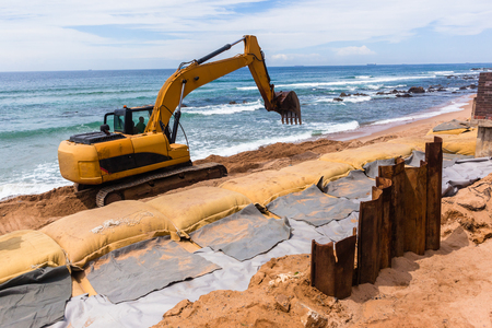 Construction excavators machines on beach water line coastline building repairs with sandbags buffer on sand dunes to protect road from ocean storms.の写真素材