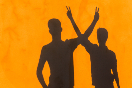 Teenager boy's body profiles and hands signals shadow on yellow textured wall with attitude abstract message.の写真素材