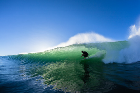 Surfing surfer tube rides ocean wave morning silhouetted water action photo unidentifiedの写真素材