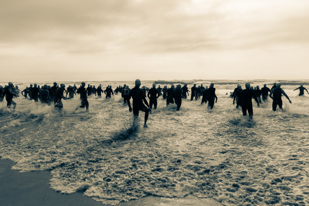 Triathlon beach athletes silhouetted swim race start in ocean water course at dawn sunriseの写真素材