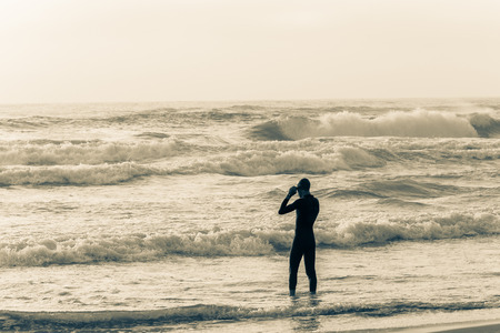 Triathlon beach athlete silhouetted swim preparation for race start in ocean water course at dawn sunriseの写真素材
