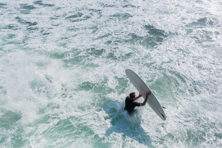 Surfers with surfboards jump off beach pier jetty into ocean water for quick entry to go surfing ...