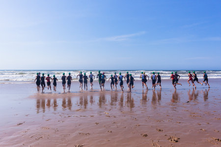 Triathlon National Champs Durban, South-Africa - March 24 , 2019 : Athletes teenagers runnning off beach entering ocean wave surf for swimming leg start of triathlon race.のeditorial素材