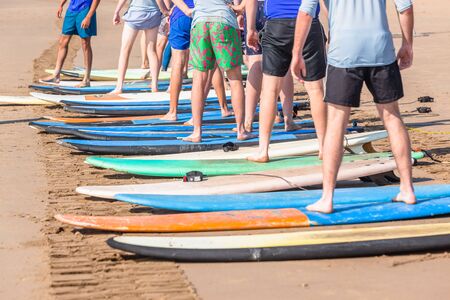 Surfing lessons on beach young men legs standing on surfboards basic wave riding skill next to ocean water shoreline.の写真素材