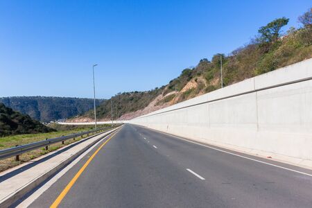 New road highway with concrete walls and pool lanes winding up down through rural valley landscape