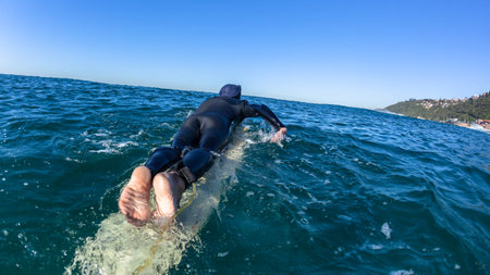 Surfing Surfer padddling ocean sea waters back to wave peak swimming closeup behind horizon perspective photo  coastline.のeditorial素材