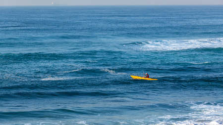 Morning beach entry fisherman mature Caucasian paddling out towards ocean sea back line in yellow kayak canoe a panoramic landscape.の写真素材
