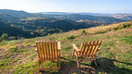 Two wood chairs together overlooking scenic mountains valley with forest trees in afternoon blue skyのeditorial素材