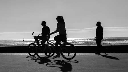 Cycling Couple silhouetted unrecognizable Man Woman riding bicycles on beach front promenade with ocean waves background .の写真素材