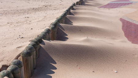 Beach sand blows over low placed wood roles onto  promenade pathway in mounds of sandy piles of grain during season of high winds.の写真素材
