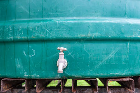 Large green water tank closeup of tap and rusted stand in rural farmlands countryside.