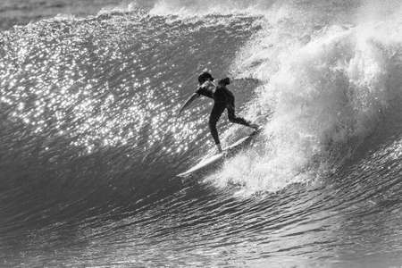 Surfing surfer rides sunlight reflecting ocean wave unrecognizable male rear behind action black and...