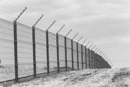 Security fencing with electrified wires along property boundary outdoors in black and white...