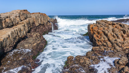 Rocky coastline ocean sea water rushing crashing up rock gulley crevace  sea water spray power along...