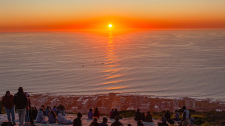 People  sitting on Signal Hill watching viewing sun down a scenic moment on the horizon over the Atlantic ocean Cape-Town.の写真素材