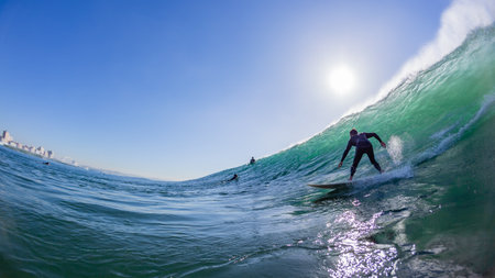 Surfer surfing silhouetted rides Durban ocean wave morning light a rear behing swimming  water action photograph with beach building landscape perspective.の写真素材