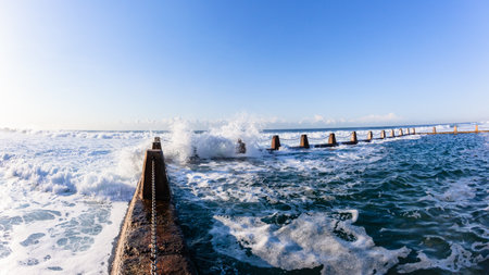 Beach Tidal Swimming Pool with Ocean waves crashing over chain wall.の写真素材