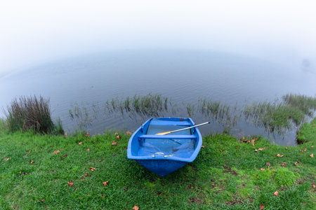 Blue Paddle Boat along waters edge of  dam covered with cloud mist arriving over  with autumn season arriving in countryside holiday landscape.の写真素材