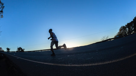 Marathon runners silhouetted morning dawn sunrise running up hill in ultra distance raceの写真素材