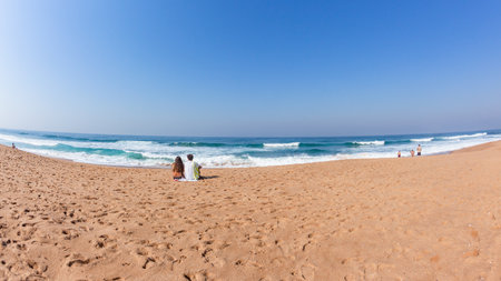 Girl Boy sitting beach sand facing blue sea ocean horizon in conversation unrecognizable persons a distant rear view photo of landscape.の写真素材