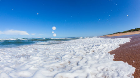 Beach ocean waves crashing onto shorebreak sand with white blue water power a close up swimmer perspective.の写真素材