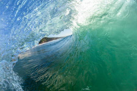 Ocean wave hollow tube crashing water lip back lit sunlight contrast a close up swimming surfer surfing perspective coastline landscape.の写真素材
