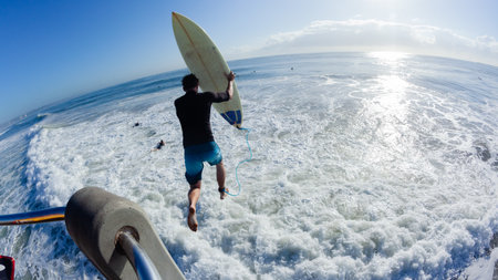 Surfer rear behind action unrecognizable teenager mid-air jumping onto white water wave with...