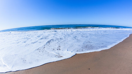 Scenic beach sea ocean with a wave white water wash along waters-edge sand shoreline a clear blue...