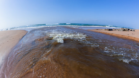 Rivermouth flowing water middle photograph out of lagoon through beach sandbar to blue sky ocean .