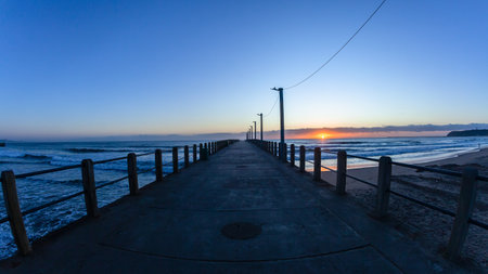 Dawn beach ocean pier jetty silhouette with horizon sunrise a scenic landscape.の写真素材