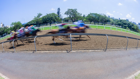 Horse racing horses jockeys motion speed blurs running action close-up track inside railing on sand poly section perspective on a clear blue day.の写真素材