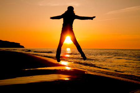 a woman takes a leap on a beach while the sun sets in the background