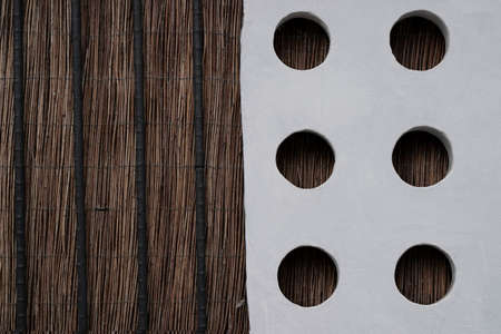 Brown wattle fence connected to a white concrete slab with round holes. . Selective focus on texture.の写真素材