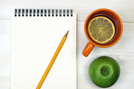 tea, green apple, pencil and notebook on a white wooden surface の写真素材