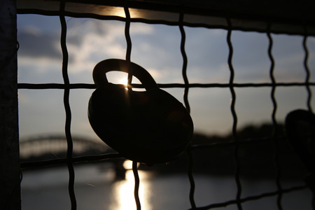 love padlock chained to a bridge with rays of the setting sunの写真素材