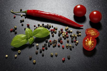 cherry tomatoes, red chili pepper, basil leaves on black backgroundの写真素材