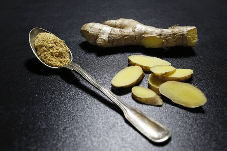 fresh ginger root and spoon with powder on black background