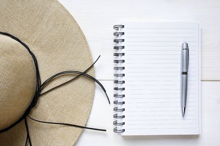 Straw hat and empty notebook on white wooden backgroundの写真素材