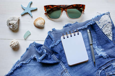 Summer planning concept- jeans shorts, sunglasses, seashells and notebook on white backgroundの写真素材
