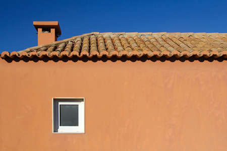 facade with window of orange vacation house with clay roof tiles against blue skyの写真素材