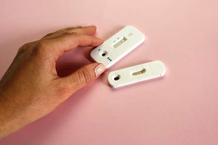 female hand holding express medical self tests on pink background