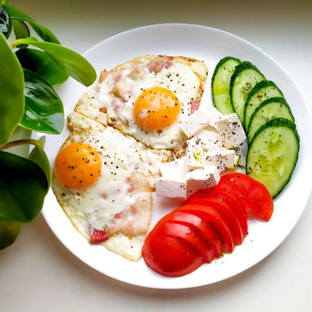 Traditional breakfast with bacon, fried eggs, cucumbers, tomatoes and feta cheese, sprinkled with basil and political olive oil.の写真素材