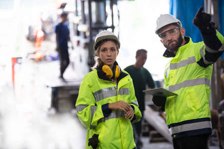 Men and female workers in factory operating machine in workshop floor.